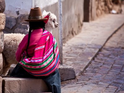 Woman in traditional clothes with lama sitting on stone in Cuzco - Peru