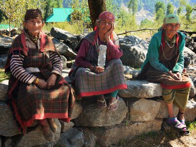 Three women in traditional clothing sat on stone wall under tree shade, India