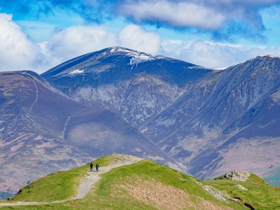 Two ramblers in distance walking pathway with view of Skiddaw mountain from atop Cat Bells, Lake District, Cumbria