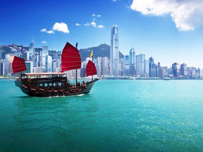 Hong Kong harbour with tradition Chinese junk ship with red sails and cityscape in background on sunny day