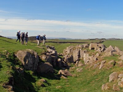 Ramble worldwide walking group standing by edge of small hill admiring rocks on Limestone Corner on Hadrian's Wall national trail, England