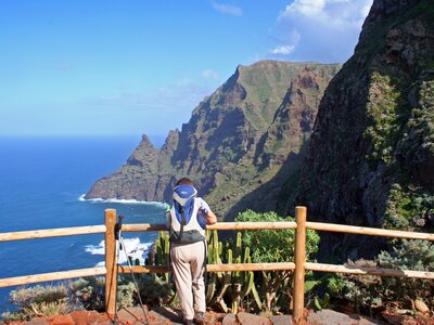 Male hiker leaning against wooden post admiring coastal view of Tenerife, Canary Islands, Spain