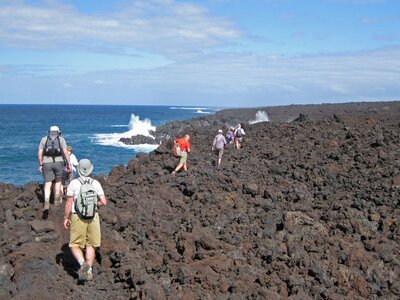 Walking group on Ramble Worldwide walking holiday traversing over igneous rock near the sea in Lanzarote, Parque National de Timanfaya