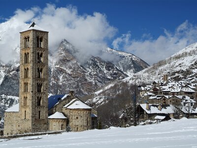 Church of Sant Climent de Taüll, Spain catholic church in winter with nearby houses and a snow-capped mountain in the background