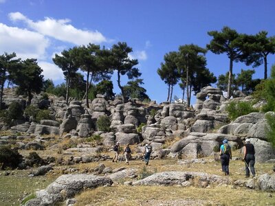 Walking group on St Paul's trail in Selge with interesting smooth rock formations and tall pine trees in distance, Turkey