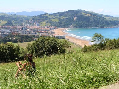 Woman sat in grass on hillside overlooking scenic beach and town view of Zarautz, Spain
