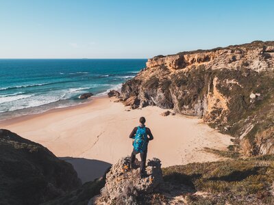 Backpacker looking at sandy beach from above with cliff edge wrapping around, Rota Vicentina Fisherman trail, Algarve , Portugal