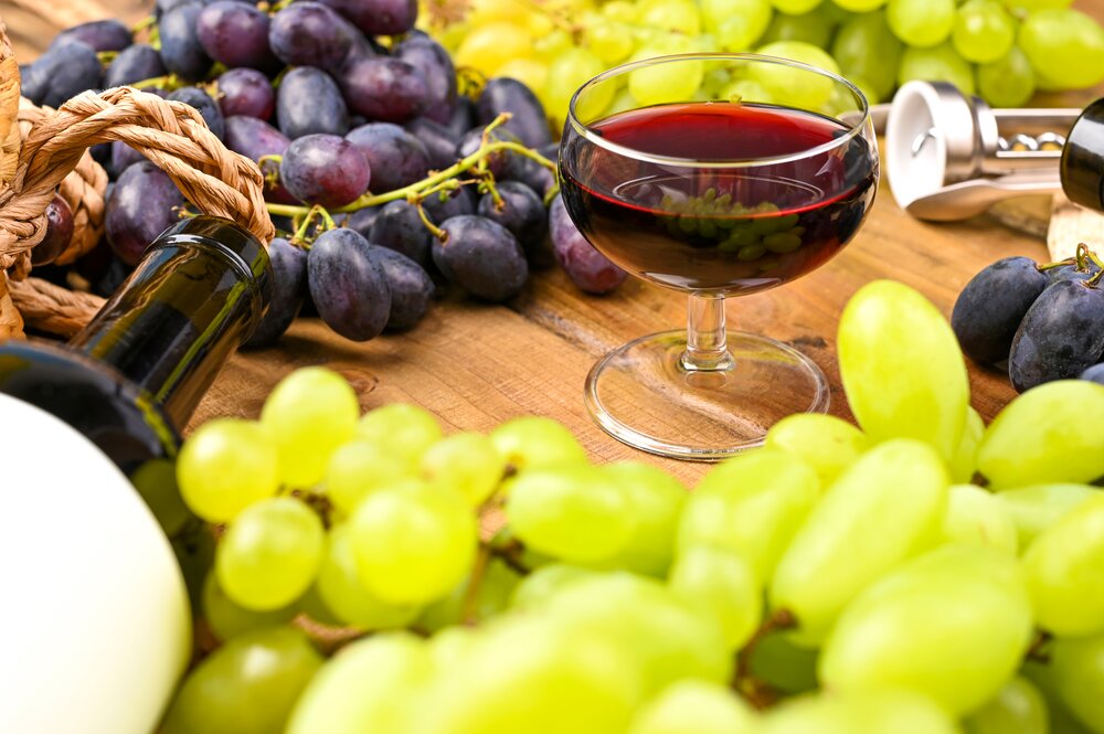 Italy festivals blog -- A glass of red wine and grapes. Traditional Italian holiday and summer holidays, Ferragosto harvest festival. Red and white wine on a wooden background and grapes.