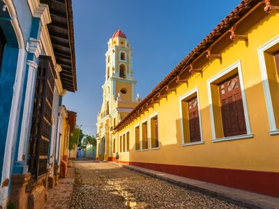 Cobbled street between pastel-hued houses and a church in Trinidad, Cuba