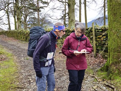 Man and woman on Ramble Worldwide Navigation & Hill Skills course reading map in Lake District along pathway
