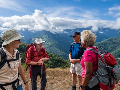 Close-up of small group of people on a Ramble Worldwide walking holiday conversing with smiles and backdrop of green mountain range of Picos De Europa in Spain on sunny day with white and blue sky