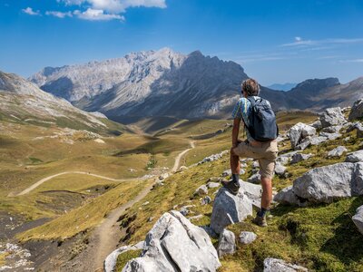 Person on Ramble Worldwide walking holiday leaning on rock admiring vast scale of Picos De Europa mountain range on sunny day with blue skies, Spain