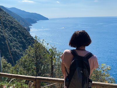 Lady on Ramble Worldwide walking holiday leaning on wooden fence admiring coastal view of green mountains and blue sea on sunny day in Monterosso, Italy