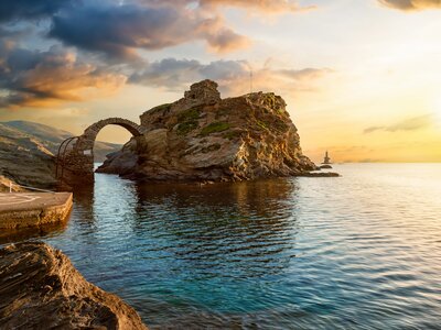 Old arched stone bridge leading to the ancient Castle of Andros island at the Cyclades of Greece during summer sunrise
