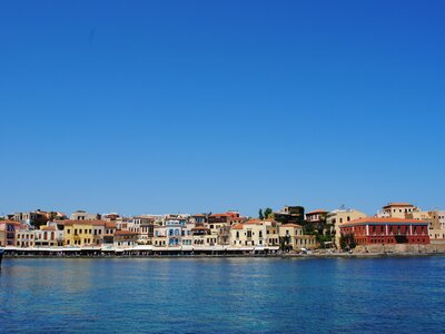 Line of colourful buildings near body of blue water during daytime with clear blue skies, Chania, Crete, Greece