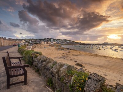 Bench overlooking beach with soft low sun glowing across sea and land at St Marys harbour in the Isles of Scilly, England