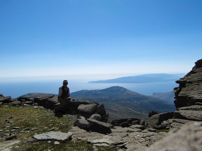 Man sat on rock near cliff edge at Mt Ochi with view of mountainous landscape and seaview upfolding behind him, Greece