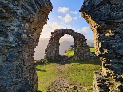 Stone arch atop Welsh peak with sun casting warm low and long shadows, walkways of Castell Dinas Bran, Wales