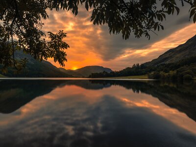 View from Crummock Water shore of sunsetting behind Lake District fells with reflection