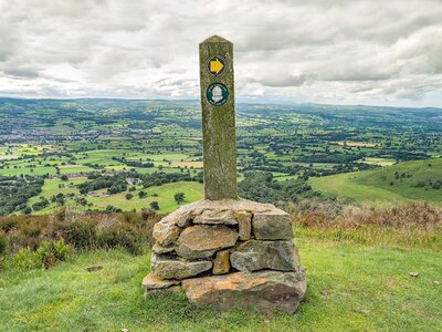 Offa's Dyke Path wooden stake signpost cemented in stone with countryside landscape in background, Wales, UK