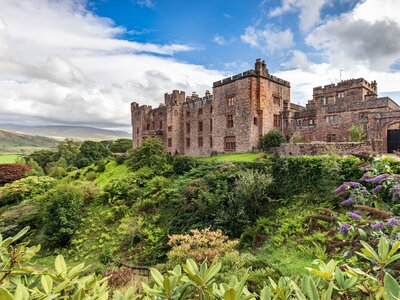 Muncaster Castle overlooking the Esk river near the coastal town of Ravenglass in Cumbria with colourful plants in foreground, England