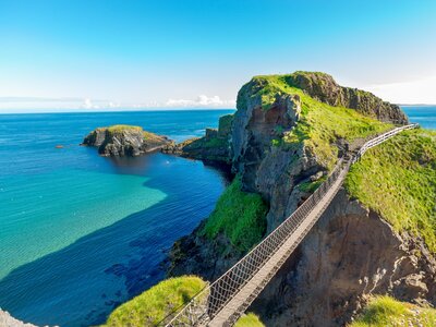High view of Carrick-a-Rede rope bridge and green coastal cliff in Northern Ireland