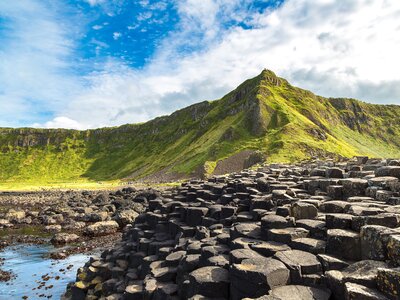 Multiple polygonal-shaped basalt stone columns with green rocky peak in distance, Giant's Causeway on a sunny summer day, Northern Ireland