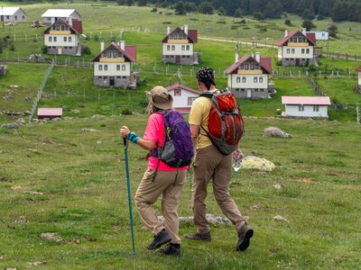 Couple trekking across grassy field with houses in background, Kasimlar, Ankara Province, Turkey