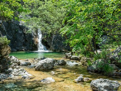 Orlias Waterfall with a green pool and green trees growing by water's edge providing shade at Mount Olympus, Greece