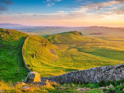 Golden sunlight at Hadrian's Wall Caw Gap casted over green hills with roman wall casting long shadows from ridge