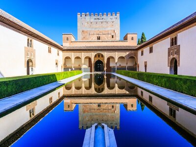 Symmetrical centre view of Alhambra Palace fortress reflected in long body of still water mostly covered in shadow with sun shining on Alhambra Palace, Granada, Spain