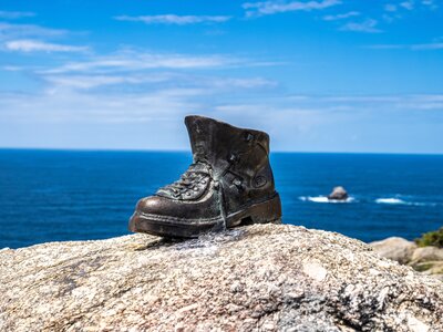 Metal used boot placed on rock at the end of Saint James Way in Finisterre Fisterra Camino de Santiago with blue sea and sky in background, Spain, Europe