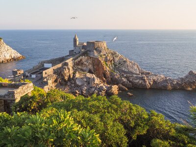 Sunset in the Gulf of Poets among beautiful landscape of Porto Venere with Ruins of Doria Castle, church of Saint Peter on a steep cliff and Mediterranean sea and seagulls flying nearby, Palmaria Island, Italy