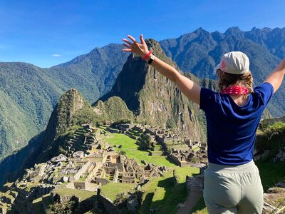 Hiker atop mountain edge of Machu Picchu with arms up in air embracing view of Incan ruins and mountainous landscape, Peru, South America