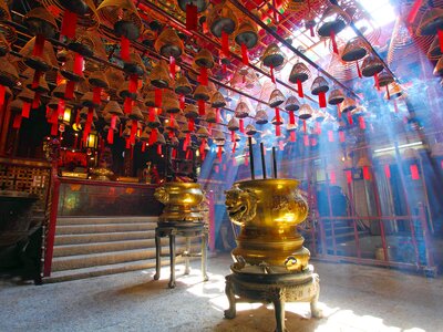 Man Mo Temple in Hong Kong with rays of sunlight beaming through into incense filled room and red paper hanging overhead