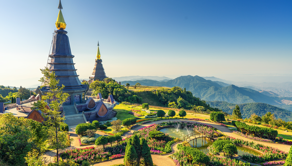 Two pagoda at the Inthanon mountain with winding pathways surrounded by colourful flowers, plants, and trees with mountainous landscape and hazy blue sky in distance, Chiang Mai, Thailand