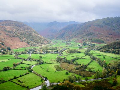 Expansive view of green fields and orange-tinted fells of Rosthwaite and the Borrowdale valley in the Lake District on cloudy day, Cumbria, UK