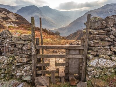 Wooden stile and handmade stone wall with fells in background, Borrowdale, Lake District