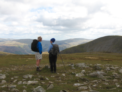 Walking couple pausing on hike amidst Lake District fells looking at mountainous scenery