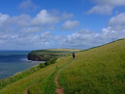 Couple hiking UK national trail coast to coast route following dirt pathway on slanted grassy hill with sea view, from St Bees to Robin Hoods Bay 
