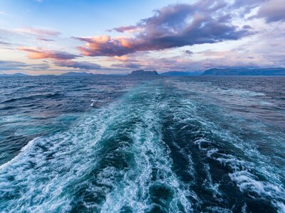 Fred Olsen cruise ship trail in Norwegian sea with soft pink and orange lit clouds hanging in sky in distance