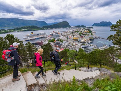 Ramble Worldwide walking group descending stone stairway from Aksla hill with view of Alesund port town and Norwegian fjords in distance