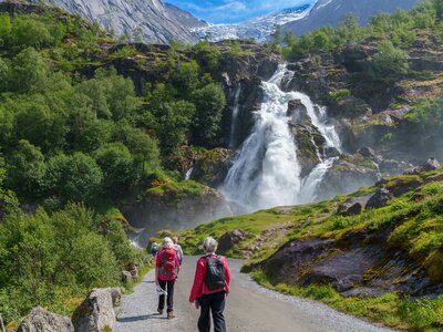 People on Ramble Worldwide cruise and walk holiday The Fjords of Norway walking towards Briksdalsbreen waterfall in distance with glacier in far background, Norway, Europe