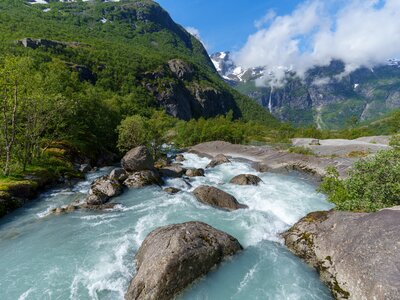 Glacial water from Briksdalsbreen glacier flowing past boulders with scenic green mountainous landscape in background, Norway