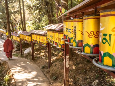 Buddhist monk walking in Kora circuit near Buddhist prayer wheel with engraved in Sanskrit, McLeod Ganj, India