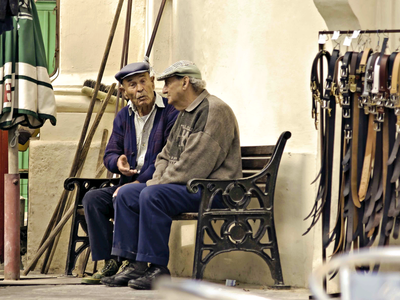 Two elderly men sat on a bench on a street in conversation, Gozo island based in the Mediterranean Sea