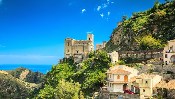 Church of St. Nicolo atop hill with houses nearby nestled into mountainside and blue sea viewed in distance near Taormina, Sicily, Italy